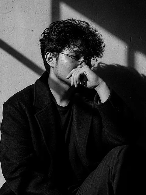 Black and white portrait of Lawrence Buena sitting against a sunlit wall